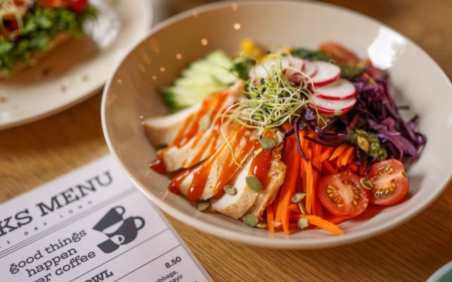 A vibrant salad bowl featuring fresh vegetables and grilled chicken on a wooden table.