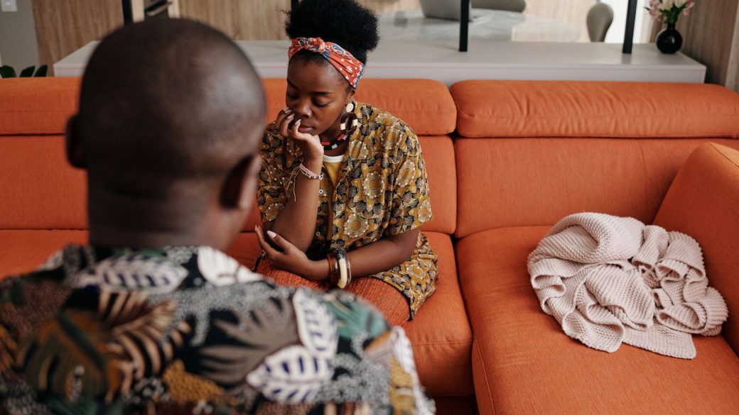 A thoughtful couple engaged in a deep discussion on a vibrant orange sofa in a modern living room.