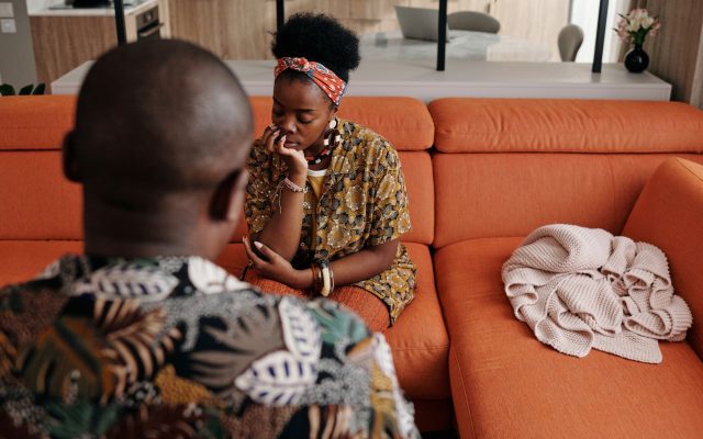 A thoughtful couple engaged in a deep discussion on a vibrant orange sofa in a modern living room.