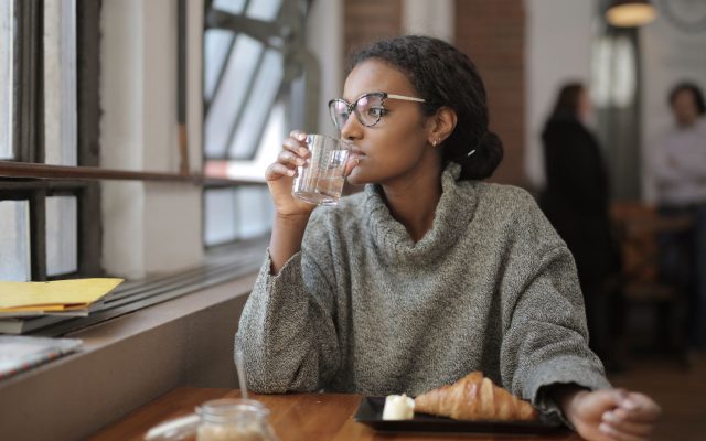 African American woman sipping water with a croissant at a cafe. Cozy indoor setting.