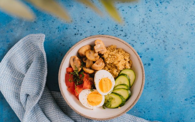 A delicious and healthy breakfast bowl featuring quinoa, boiled eggs, vegetables on a blue background.