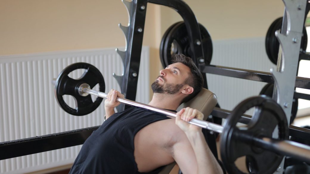 Adult man performing bench press exercise with barbell in a gym setting, showcasing strength and fitness.