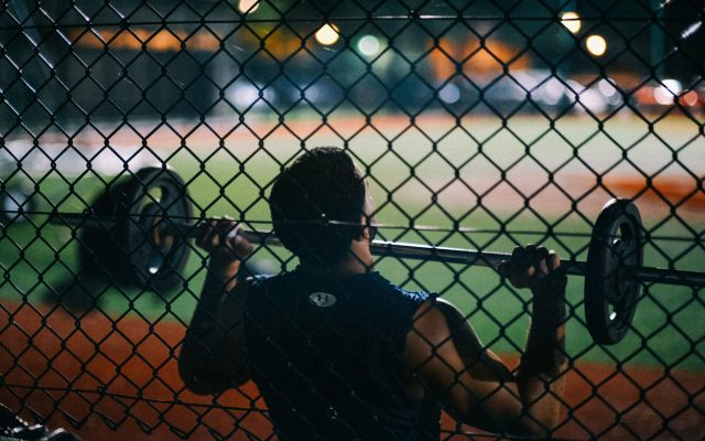 A man lifting weights behind a chain fence at night, showcasing strength and fitness.