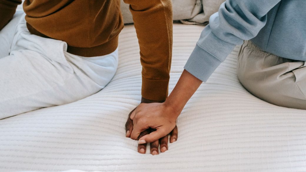 Crop faceless African American couple sitting on bed back to back and holding hands