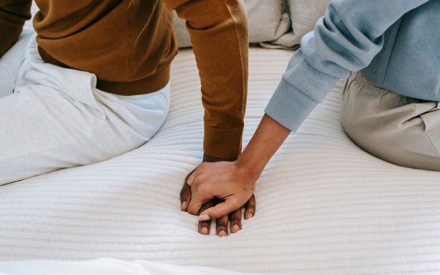 Crop faceless African American couple sitting on bed back to back and holding hands