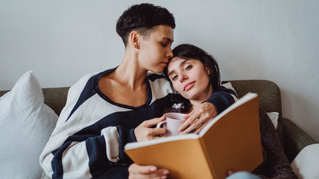 A loving couple enjoying quiet time together with a book and coffee on the sofa.