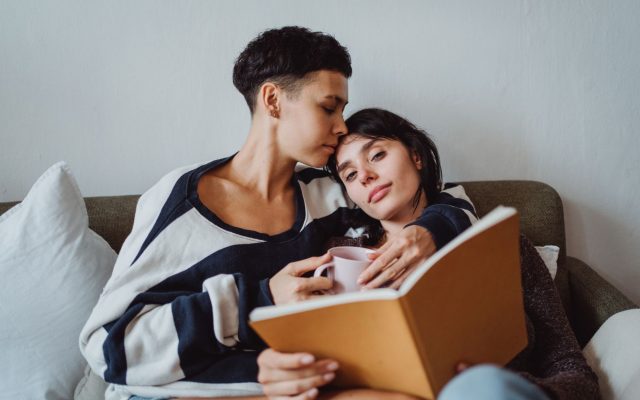 A loving couple enjoying quiet time together with a book and coffee on the sofa.