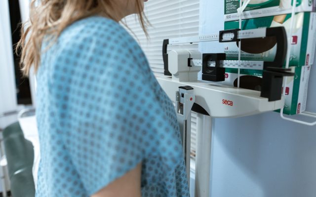 Adult female using a medical weighing scale in a healthcare setting.