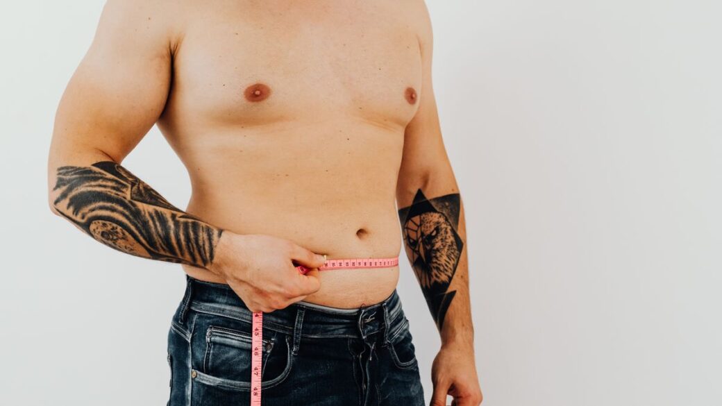 Man measuring his waist with a tape measure to track belly fat