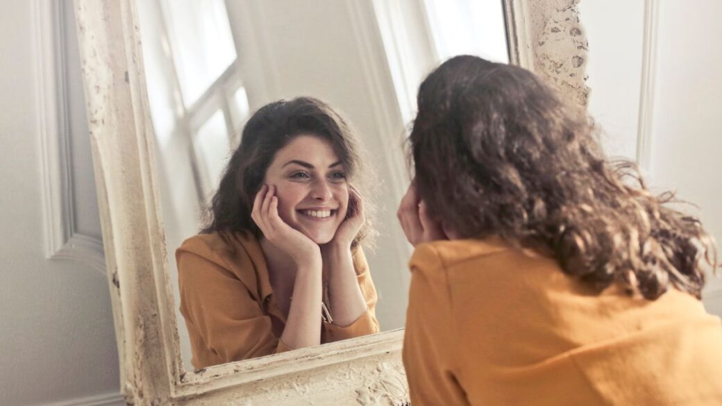 Confident woman smiling at her reflection in a mirror, a sign of healthy self-esteem