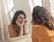 Confident woman smiling at her reflection in a mirror, a sign of healthy self-esteem