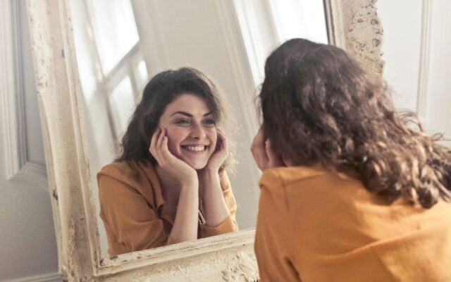 Confident woman smiling at her reflection in a mirror, a sign of healthy self-esteem
