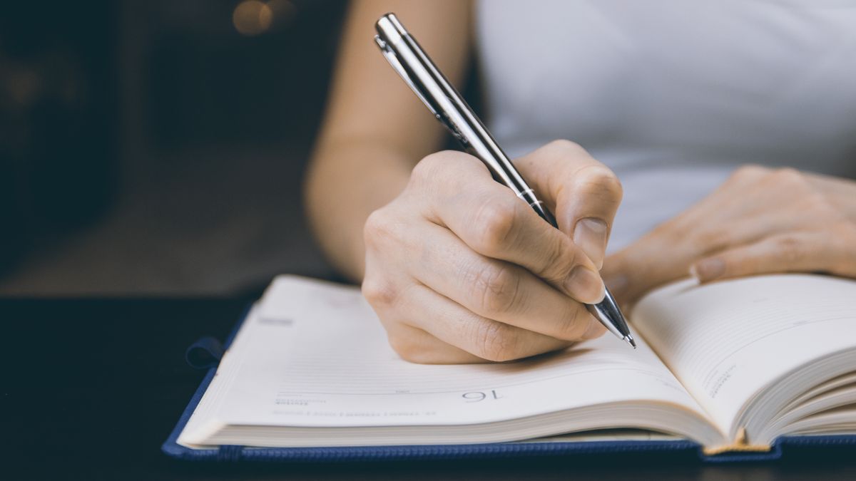 A person writing in a notebook to track their eating triggers