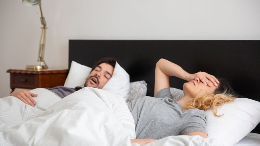 Woman covering her ears while her partner snores in bed