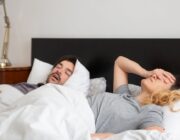 Woman covering her ears while her partner snores in bed