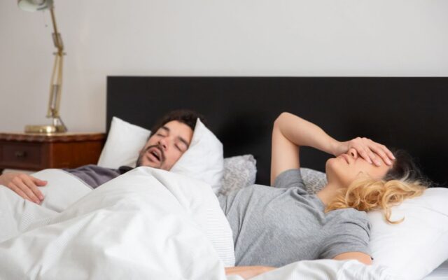 Woman covering her ears while her partner snores in bed