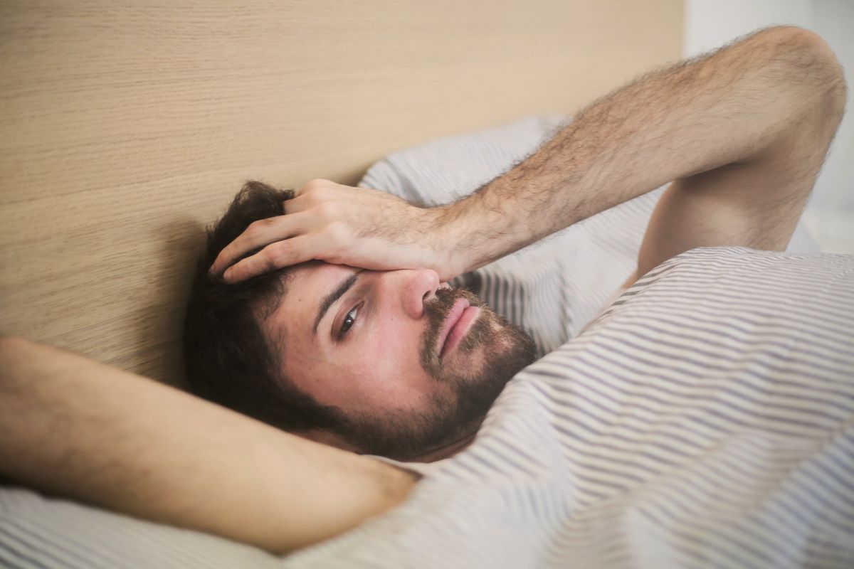 Tired man lying awake in bed in the morning after poor sleep