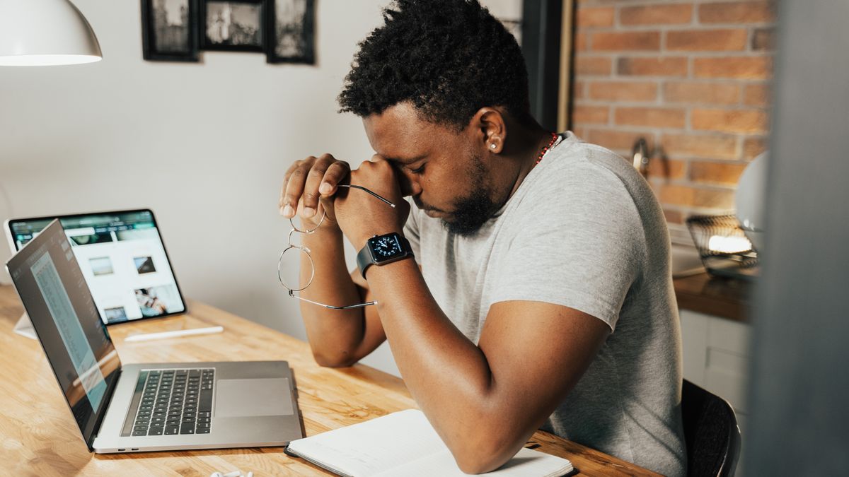 Exhausted man showing signs of burnout rubbing his eyes at his laptop