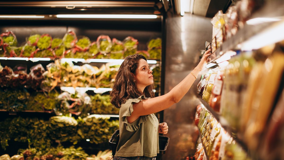 Woman experiencing decision fatigue while choosing between products in a supermarket aisle