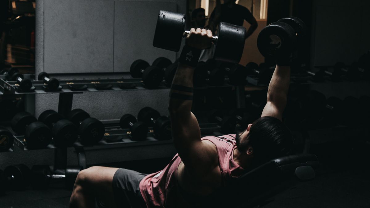Man doing an evening dumbbell workout in a dimly lit gym, weighing morning vs evening workouts
