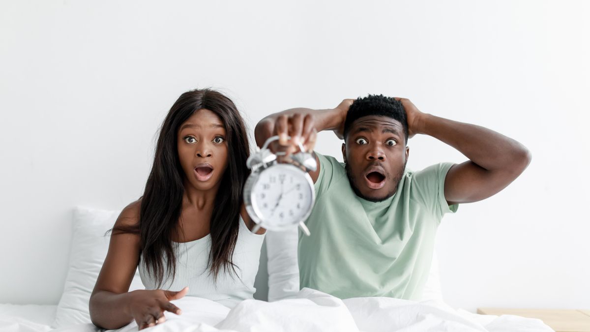 Couple asleep in bed past their alarm clock, oversleeping on a weekend morning