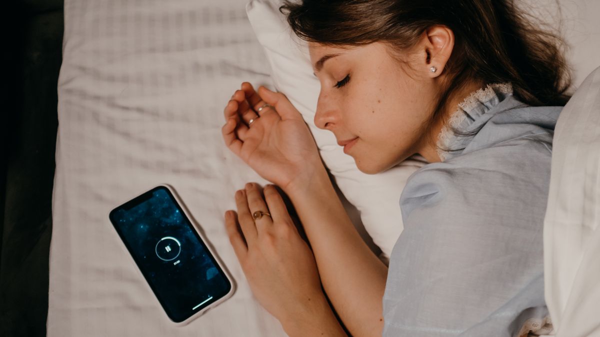 Woman asleep in bed beside her phone after oversleeping through the morning