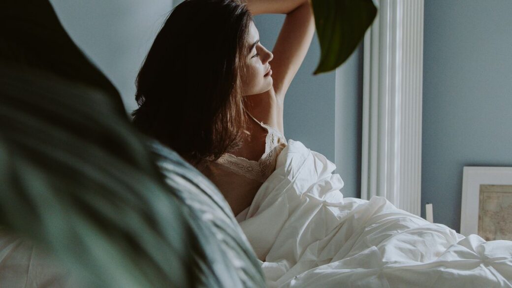 Woman waking up in a bedroom in morning light, illustrating chronotype and sleep timing
