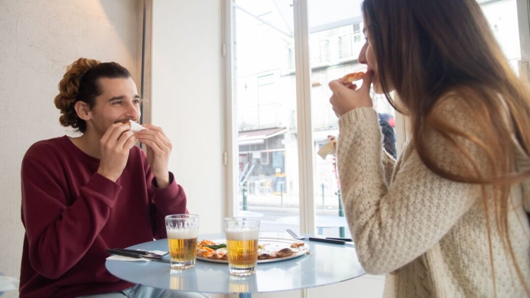 Man and woman sharing pizza in a restaurant, enjoying a planned cheat meal