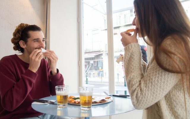 Man and woman sharing pizza in a restaurant, enjoying a planned cheat meal