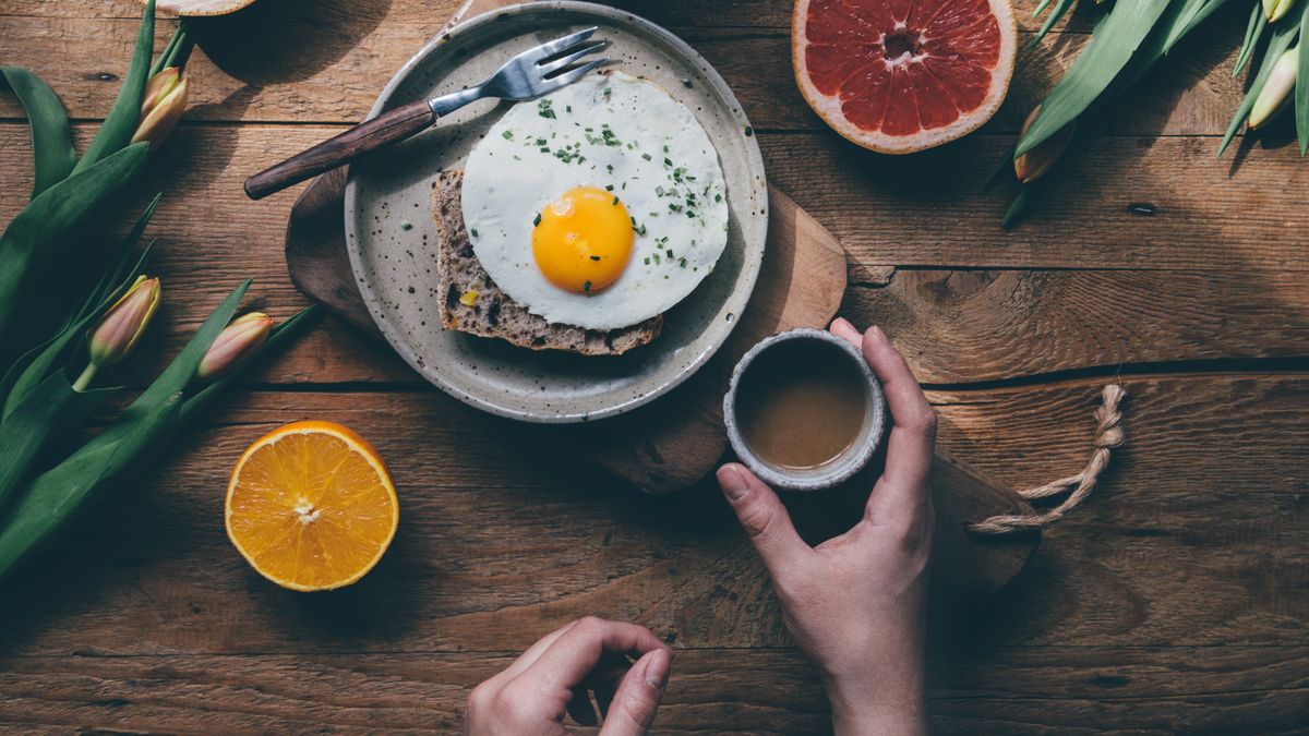 Woman having breakfast with coffee, eggs, and fruit at a wooden table