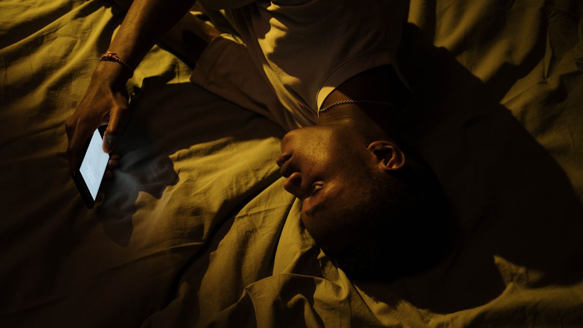 Man lying awake in bed at night checking his phone before the workweek