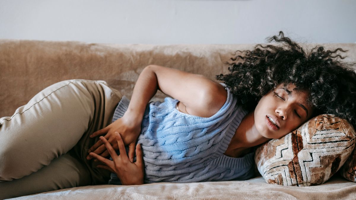 Woman with lower abdominal pain from a urinary tract infection resting on a couch