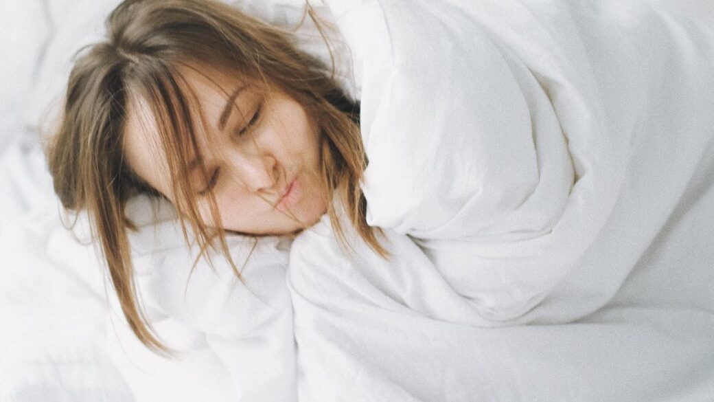 Woman sleeping peacefully under a heavy white blanket in bed