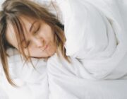 Woman sleeping peacefully under a heavy white blanket in bed