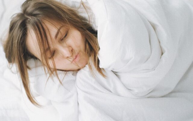 Woman sleeping peacefully under a heavy white blanket in bed